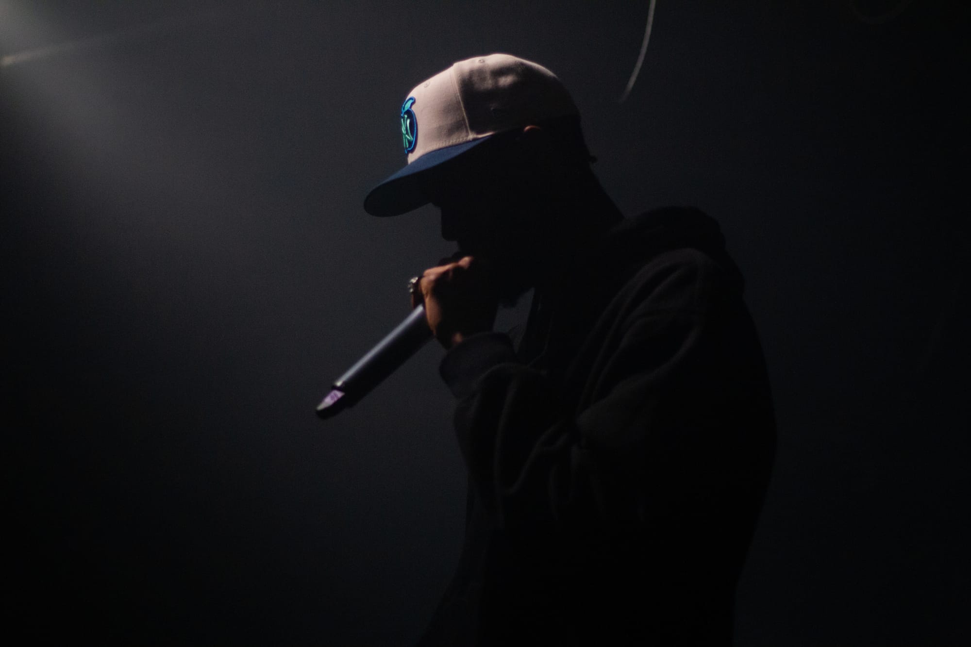 Sainte at Clint's Festival performing in a dark setting with light shining on the front of his face 