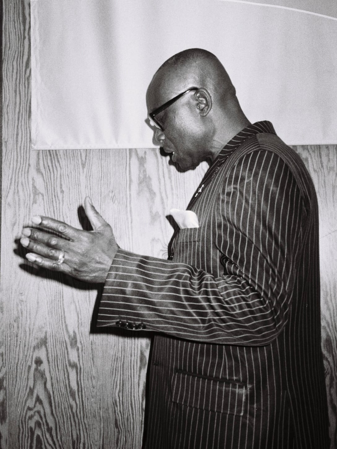 Black-and-white side profile of a man in a pinstripe suit gesturing with his hands while speaking.