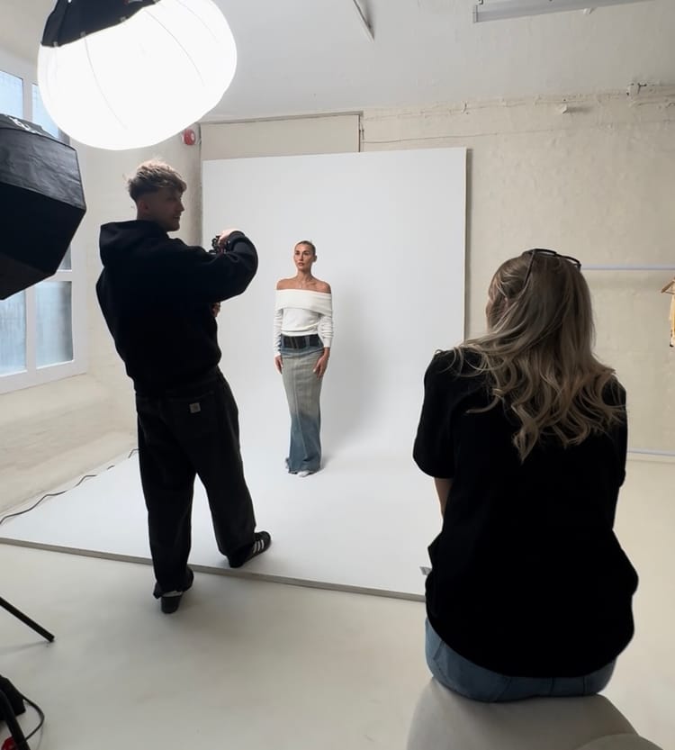 Behind-the-scenes of a fashion photoshoot with a photographer shooting a model in front of a white backdrop.